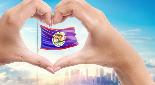 Belize national flag. Two hands forming a heart shape in front of a national flag waving in beautiful clouds. Belize national flag behind the heart shape hand.
