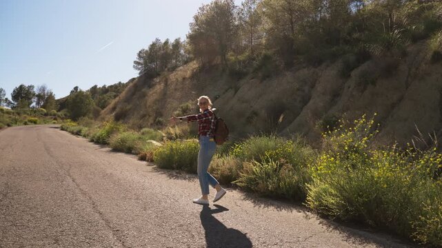 Female backpacker stand beside an empty countryside road wait for ride. Inspiring concept of new beginnings, adventure, travel journey, self discovery, freedom, independent travel, exploring world