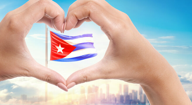 Cuba national flag. Two hands forming a heart shape in front of a national flag waving in beautiful clouds. Cuba national flag behind the heart shape hand.
