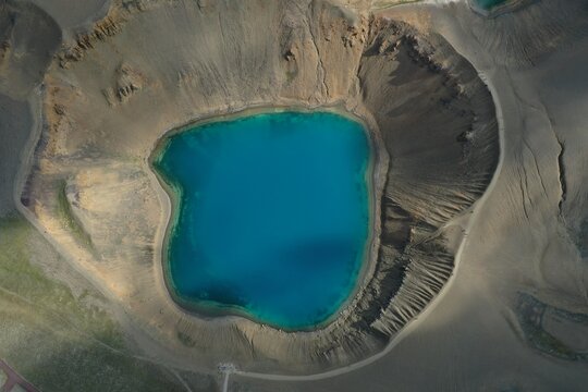Aerial view of the vibrant blue Viti crater lake at Krafla, surrounded by rugged volcanic slopes and dark earth in Reykjahlid, Thingeyjarsveit, Iceland.