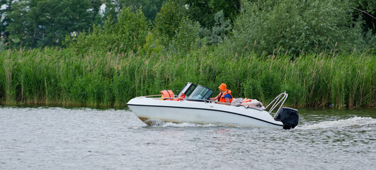 Small speedboat moves quickly on a lake past lush green shore vegetation. Perfect for themes of active lifestyle, weekend leisure, nature travel, and river navigation. Photo © slexp880