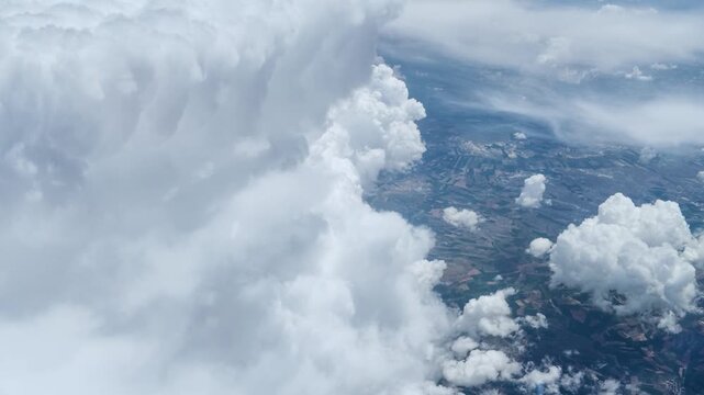 Cinematic aerial footage of scenic cloudscape. High altitude view from airplane window showing massive white cumulus clouds over terrain. Professional atmospheric stock video.