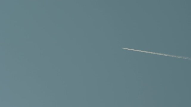 Jet airplane leaving long contrail across blue sky