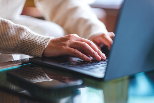 Closeup image of a woman working and typing on laptop computer with mobile phone on the table