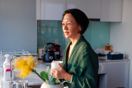 Woman in robe drinks coffee in modern kitchen.