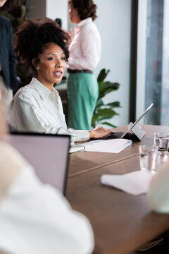 Businesswoman at meeting, typing on tablet, with colleagues present.