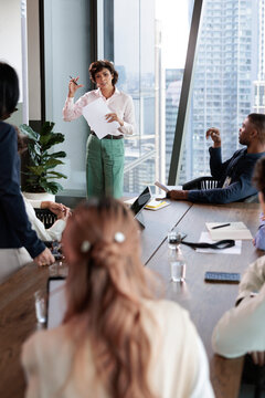Businesswoman presents to diverse team in modern office.