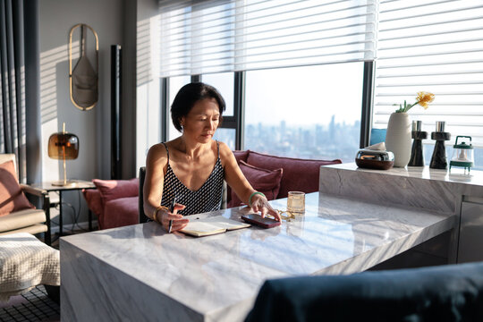 Woman writing in notebook at marble desk in apartment.