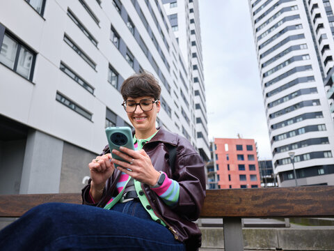 Woman smiling using smartphone on urban bench outdoors