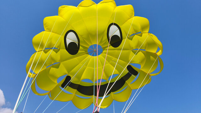 Protaras, Cyprus June 20, 2026 A bright yellow smiley face parasailing canopy against a clear blue sky, fun, adventure and excitement of a sunny beach holiday and water sports activities.