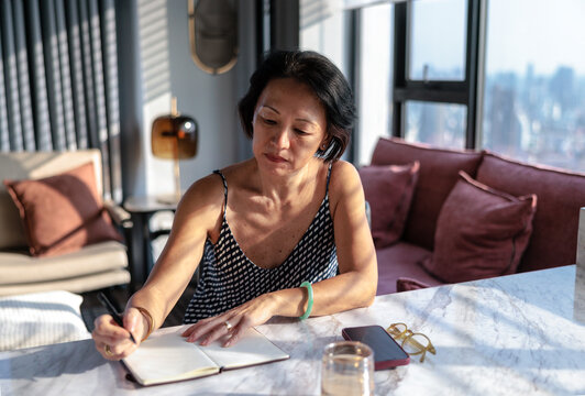 Woman writing in notebook by window with city view.