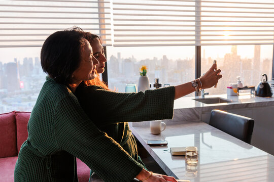 Mother and daughter taking selfie in modern apartment with city view