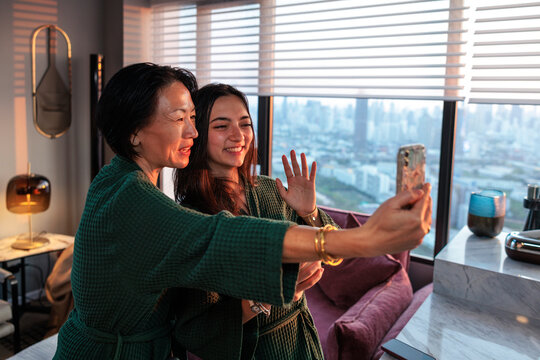 Mother takes selfie as daughter waves at phone by city window view
