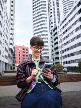 Woman smiling using smartphone on urban street bench