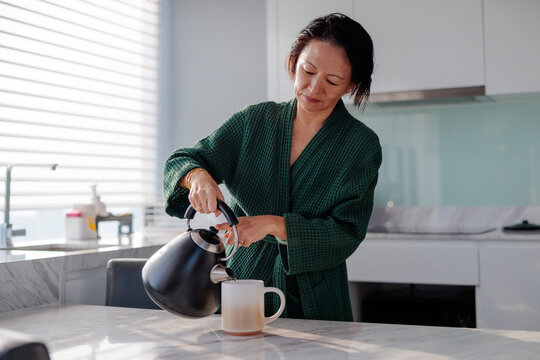 Woman in robe pours hot water into mug.