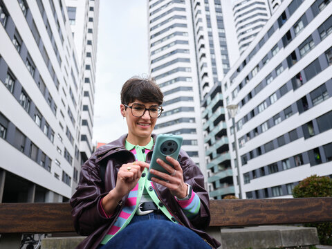 Woman smiling using smartphone sitting urban bench