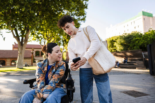 Young disabled woman in wheelchair looking at phone being shown