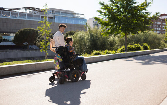 Young man assisting woman in electric wheelchair outdoors