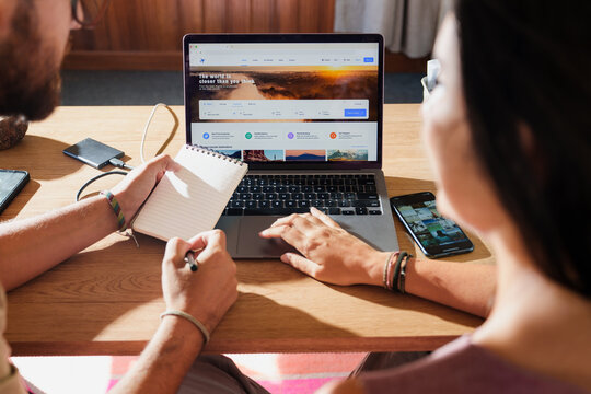 couple Searching Flights on Laptop with notebook on Desk