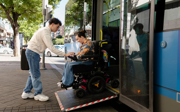 Young man helping woman with power wheelchair boarding bus