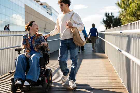 Young man assisting woman pushing power wheelchair outdoors
