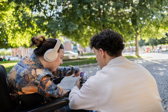 Young people sharing smartphone content listening music in park