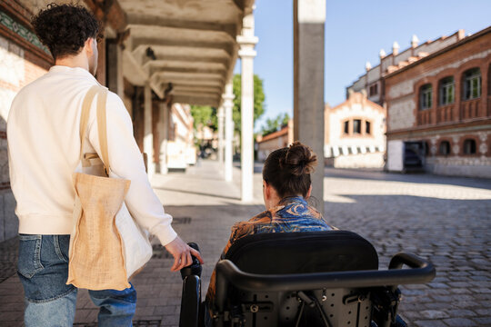 Partner pushing woman in wheelchair on city street