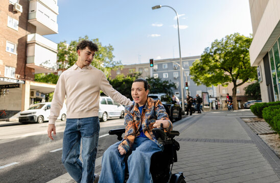 Young man assisting woman in wheelchair on urban street
