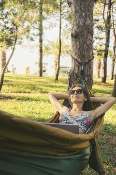 Happy Young brunette caucasian woman in hammock relax browse net work enjoy nap in park on black sea coastline on remote working holiday vacation in caucasus. Blogger travel influencer digital nomad