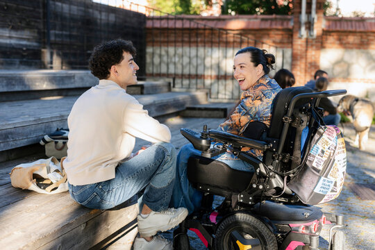 Happy young woman in wheelchair talking with friend