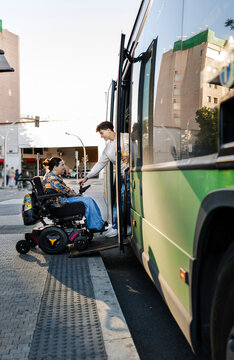 Woman in wheelchair boarding public bus with assistance