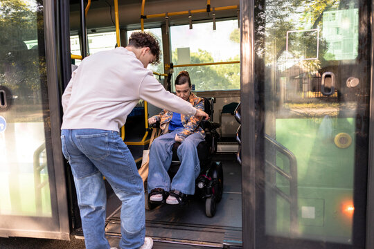 Young man assisting woman in wheelchair entering public bus