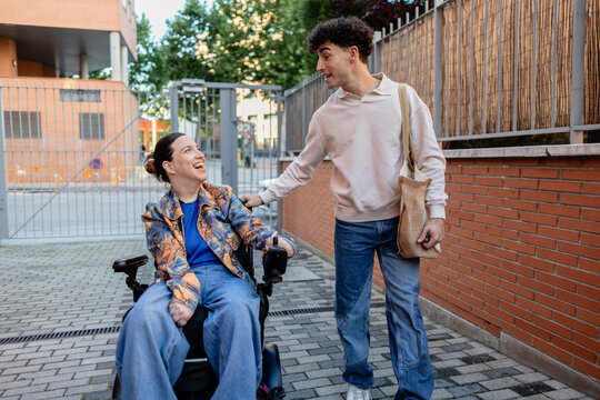 Young man pushing woman in wheelchair smiling and laughing