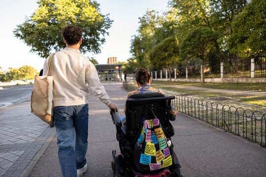 Young man pushing woman in electric wheelchair outdoors