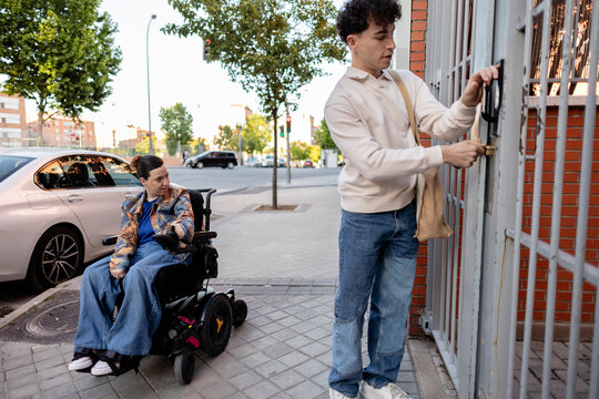 Young man opening gate for woman in electric wheelchair