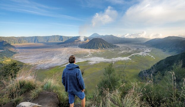Young man in front of volcanic landscape, view in Tengger Caldera, smoking volcano Gunung Bromo, in front Mt. Batok, behind Mt. Kursi, Mt. Gunung Semeru, National Park Bromo-Tengger-Semeru, Java, Indonesia