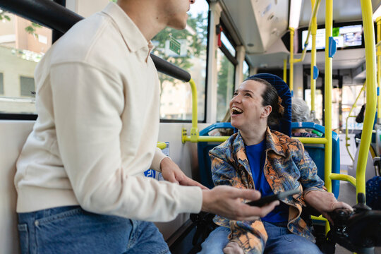 Woman in wheelchair laughing on public transport with friend