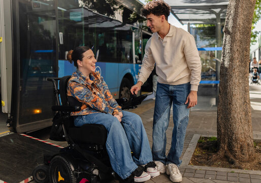 Young man assisting woman in powered wheelchair boarding bus