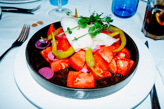 a plate of tomato salad with cod carpaccio on a table
