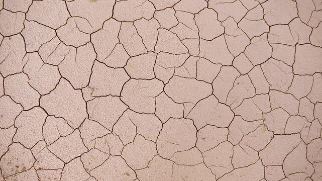 A close-up view of cracked dry earth, showing the arid texture and arid surface of a desert landscape. The ground is a mosaic of irregular polygons.