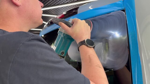 A man polishes the glass of a car with a polishing machine from small scratches with a large one. Auto glass repair, replacement. Car detailing. Hands with an orbital polishing machine. 