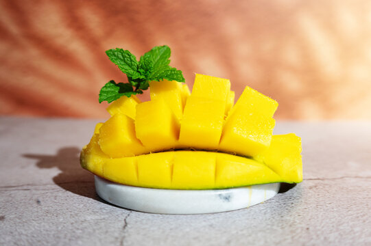 Half of a ripe mango cut into cubes against a background with sun shadows.