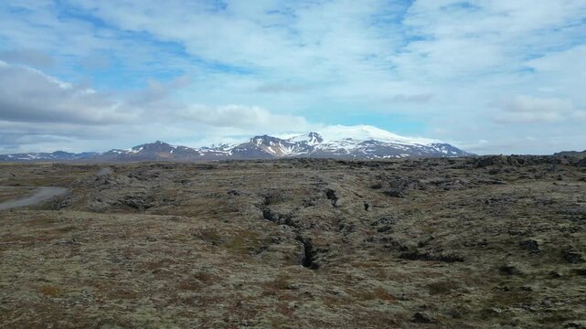 Survol des champs de lave en Islande, en direction des montagnes enneig&eacute;es en arri&egrave;re plan