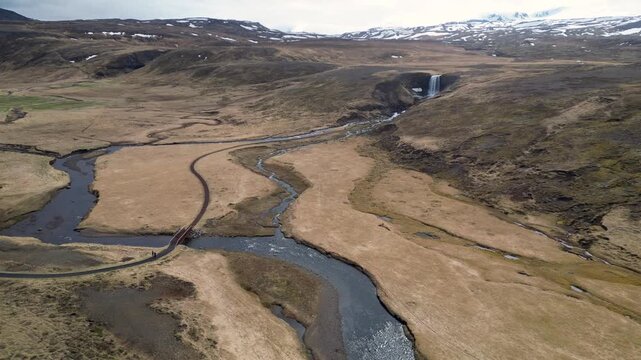 Survol de la nature au dessus dune rivi&egrave;re qui d&eacute;coule d'une cascade, avec des montagnes enneig&eacute;es
