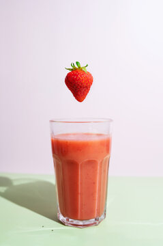 Aesthetic strawberry smoothie beverage in a glass cup under direct sunlight with berry.