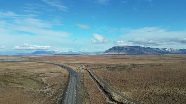 Survol d'une route qui traverse les paysages d'Islande , d&eacute;sertique et montagneux, sous un ciel bleu
