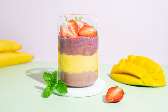 Glass of creamy berry smoothie featuring multicolored fruit layers and fresh strawberry topping.