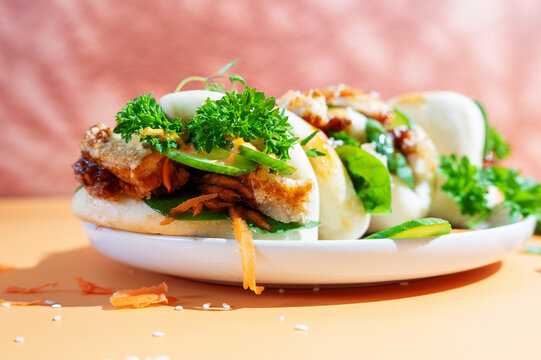 Soft steamed bao buns filled with juicy teriyaki chicken, served on a bright yellow background.