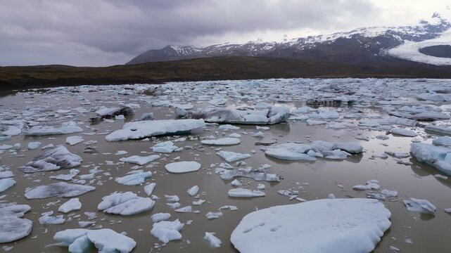 un lac marron avec des morceaux de glaces qui le recouvrent et des montagnes en fond