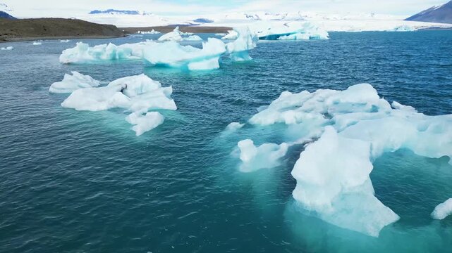survol en raz motte d'icebergs au dessus d'ne lac bleu avec un glacier en fond